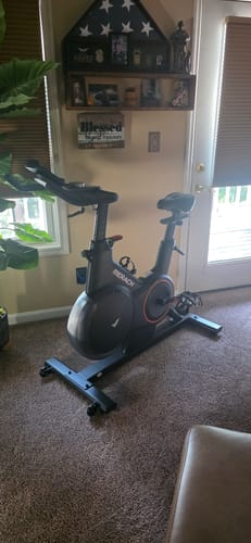 Customer's Merach exercise bike in a carpeted home living room setting.