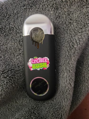 Customer's matte black MUHA Meds Live Resin vape device with Lychee Kush branding, resting on a gray textured surface.