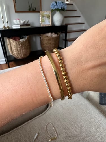 Customer's gold Marbella Cuff Bracelet stacked with other bracelets on their wrist.