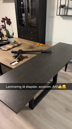 Reviewer applying Skifer matt kontaktplast on a surface, showing the dark gray slate-look finish.