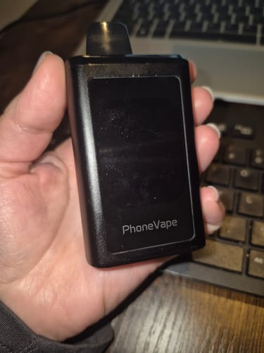 Customer's hand holding a black JNR Phonevape 30000 Puffs Disposable Vape with a dark screen in front of a keyboard.