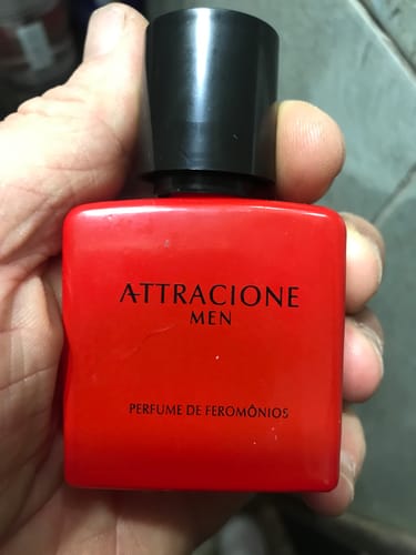 Customer's hand holding a red Attracione Men perfume bottle with black cap.