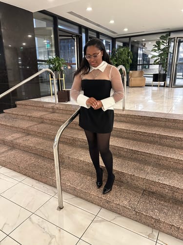 Customer's Ponte Shirting Mini Dress with shirting accents and sheer sleeves, posing on stairs.