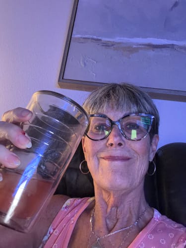 Reviewer holding a glass of clear, reddish Passionfruit THC Light Seltzer at home.