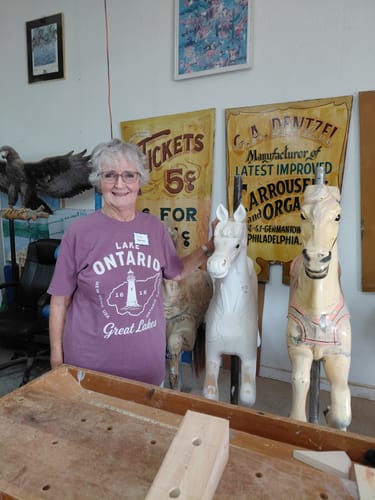Customer's mauve Lake Ontario Great Lakes t-shirt worn while standing in a wood carving shop next to carved horses.