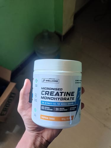 Reviewer's hand holding a jar of Wellcore Micronised Creatine Monohydrate in Tropical Tango flavor.