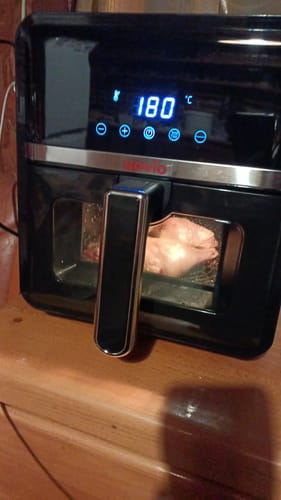 Reviewer's Novio StonePro air fryer cooking raw chicken, visible through the digital display's clear glass window.