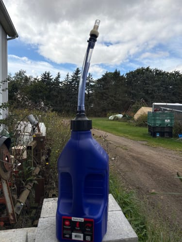 Customer's blue Tuff Jug utility container with a long, clear hose attachment, standing on concrete outdoors.