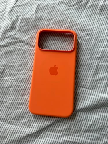 Customer's orange iPhone 17 Pro Max silicone case, front view on a striped fabric surface.