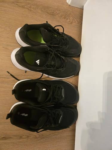 Customer's new black shoes placed next to an older, different pair of shoes on a wooden floor.