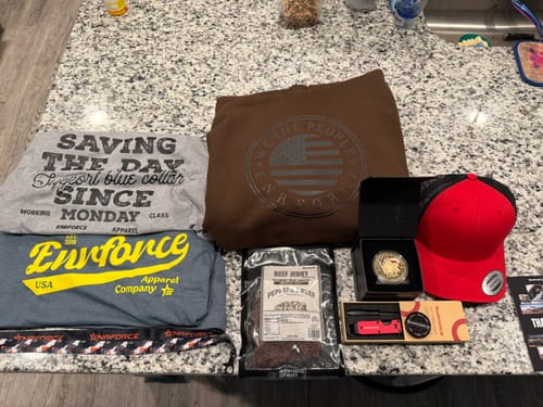 Customer's ENR#89 Exclusive Mystery Box contents including two shirts, a brown hoodie, beef jerky, a red cap, and accessories.
