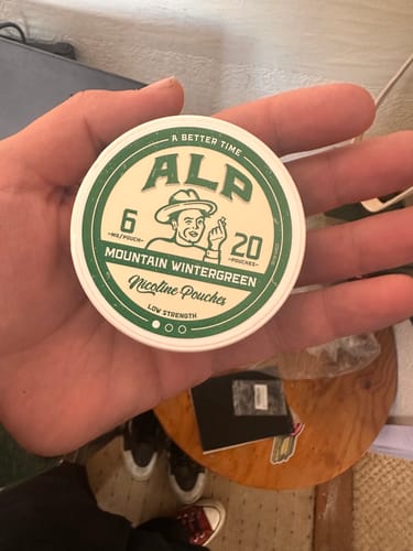 Customer's hand holding a round tin of Mountain Wintergreen nicotine pouches with green and cream branding.