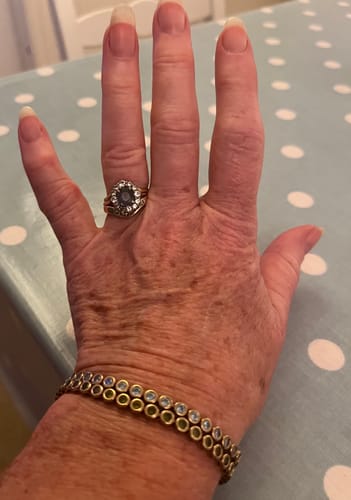 Customer's hand wearing two gold-toned Luxe Tennis Bracelets stacked together with blue cubic zirconia stones.