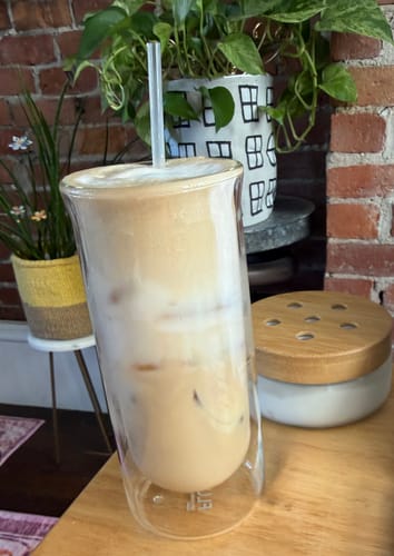 Customer's FLUR Iced Coffee Glass filled with creamy iced coffee and a straw on a table.
