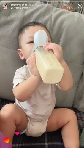 Customer's child using the grey Hegen PPSU Straw Cup to drink while sitting on a couch.