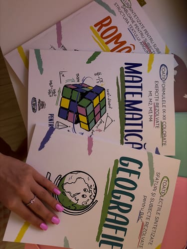Reviewer's hand holding three colorful Pachet Bacalaureat workbooks for Romanian, Math, and Geography.