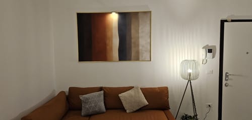 Customer's Sedimenti del Tempo painting with earthy, striped colors hung on a white wall above a brown sofa.