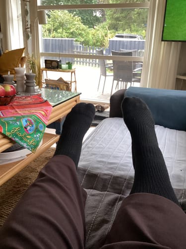 Anmelderens sorte Diasocks støttestrømper ses på fødderne, mens de slapper af i sofaen.