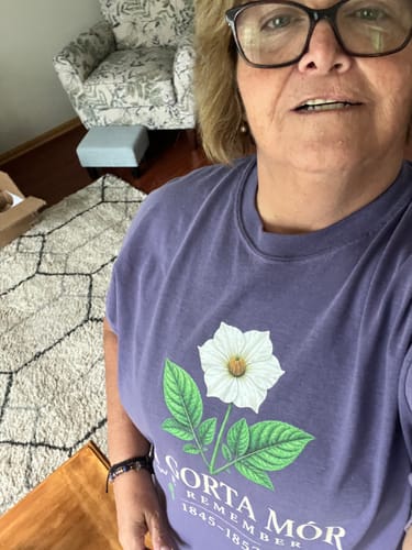 Customer's purple An Gorta Mór T-shirt featuring a white daisy design, worn in a home setting.