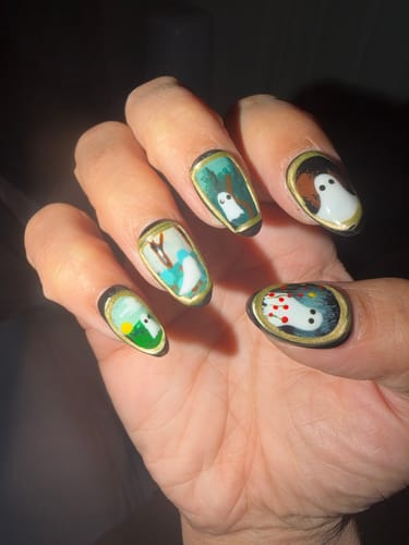 Reviewer's hand displaying Haunted Portrait press-on nails, featuring ghostly designs in gold vintage-style frames.