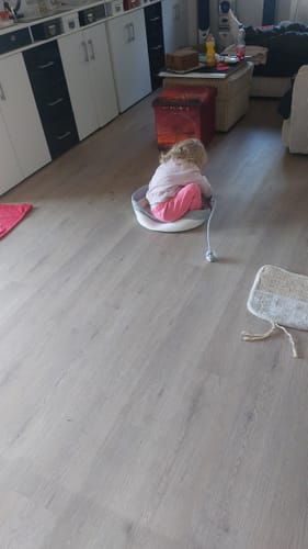 Kunde sitzt auf dem grauen Fellnest Katzenkorb in einem Wohnzimmer, da die Katzen das Körbchen nicht benutzen.