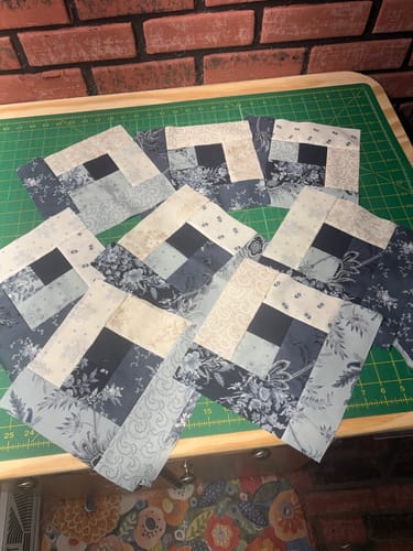 Customer's Maggie's Cabin quilt blocks in blue and cream arranged on a green cutting mat.