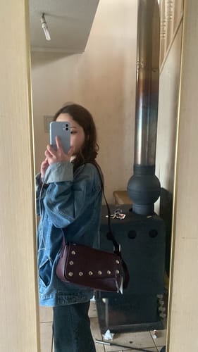 Customer's Cartera Bandolera Cruzada Éclat, a dark-colored bag with metal details, worn across the body in a mirror selfie.