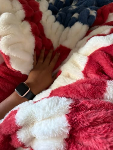 Customer's hand resting on the soft, plush red, white, and blue patriotic Hugs Flag Blanket.