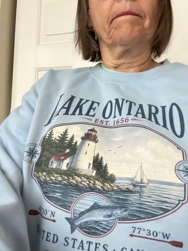 Reviewer wearing a light blue Lake Ontario sweatshirt featuring a lighthouse, sailboat, and fish graphic.