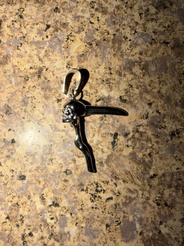 Customer's Scythe Skull Pendant shown from a top-down view against a textured stone surface.