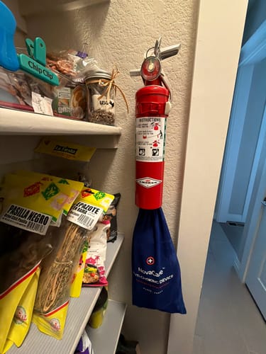 Reviewer's NovaCare Anti-Choking Device blue storage bag hanging under a red fire extinguisher in a home pantry.