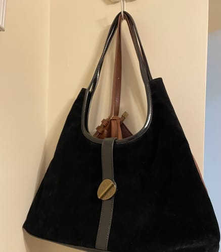 Customer's black fake suede shoulder bag with a front clasp, hanging against a plain wall.
