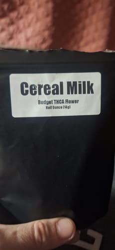 Customer's hand holding a black pouch labeled Cereal Milk Budget THCA Flower.