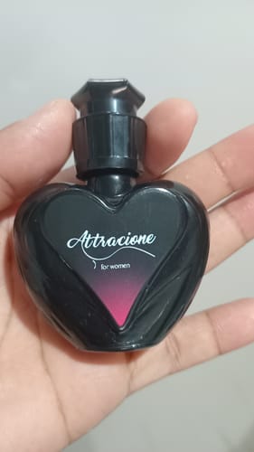 Customer's hand holding a small black heart-shaped perfume bottle of Attracione Sensual.