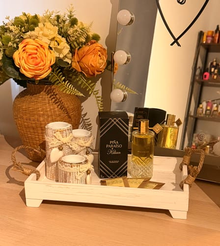 Customer's Pina Paraiso eau de parfum bottle and black packaging on a decorative tray with flowers and candle holders.