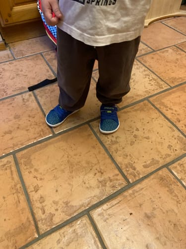 Reviewer's child standing on a tiled floor wearing Kid's Luck I blue barefoot shoes.