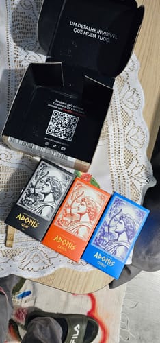 Customer's Kit Adonis perfume boxes in black, orange, and blue resting next to an open product box with a QR code.