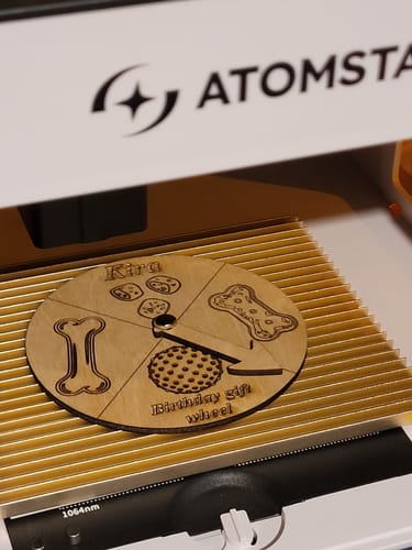 Customer's AtomStack P1 laser engraver cutting a circular wooden birthday gift wheel with etched designs.