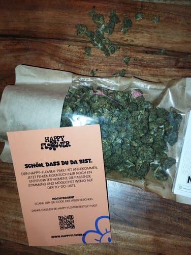 Kunden Blueberry Kush Blüten in einer offenen Packung mit beiliegender Begrüßungskarte auf einem Holztisch.