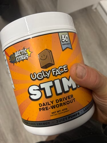 Reviewer's hand holding an orange Ugly Face Arctic Citrus pre-workout supplement container.