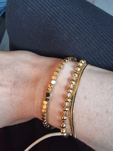 Customer's wrist wearing the gold Lexi Cube Bracelet stacked with two other gold bracelets.