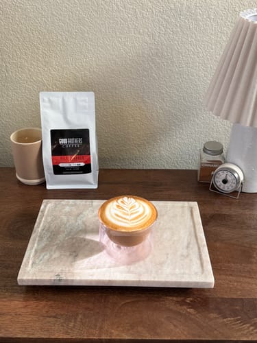 Customer's Velvet Amber Espresso Blend bag beside a latte with leaf latte art on a marble tray.