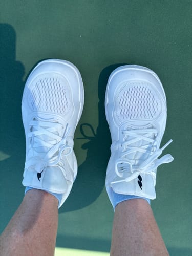 Customer's white CUURT Muuv wide toe box court shoes worn by the reviewer on a green court surface.