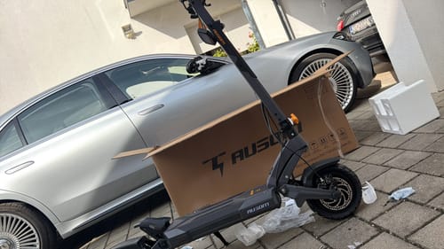 Customer's Ausom DT2 Pro E-scooter partially assembled next to its cardboard shipping box in a driveway.
