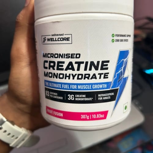 Reviewer holding a white tub of Wellcore Creatine Monohydrate with visible blue and pink branding.
