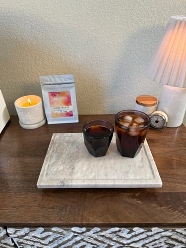Customer's Colombia Finca Milan coffee bag next to a glass of dark coffee and a glass of iced coffee on a marble tray.