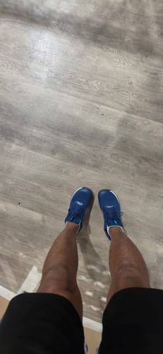 Customer's feet wearing blue CUURT Muuv court shoes, standing on a wooden floor.