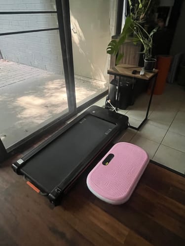 Customer's black NovaWalk W50 TrekPad placed on a floor in a studio apartment next to a pink vibration plate.