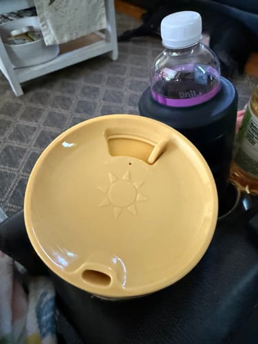 Customer's yellow ONE Lid on a cup, with a sun icon design, sitting next to a dark cup in a cup holder.