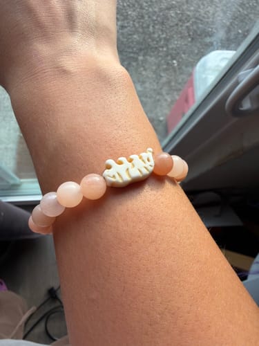 Customer's Prowl Bracelet on wrist, featuring light pink beads and a patterned charm.